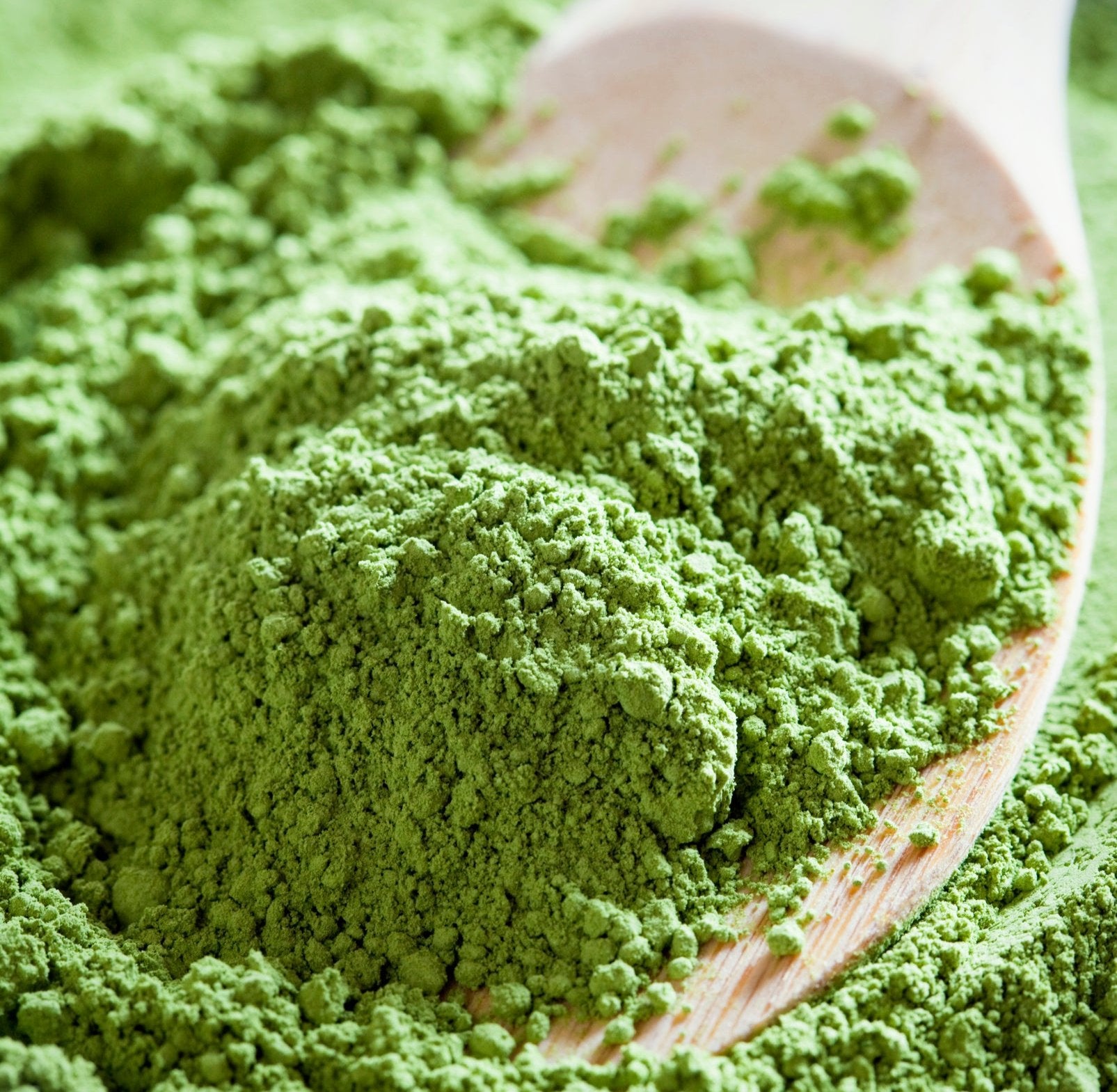 Vibrant, green close up of matcha powder laid across wooden spoon.