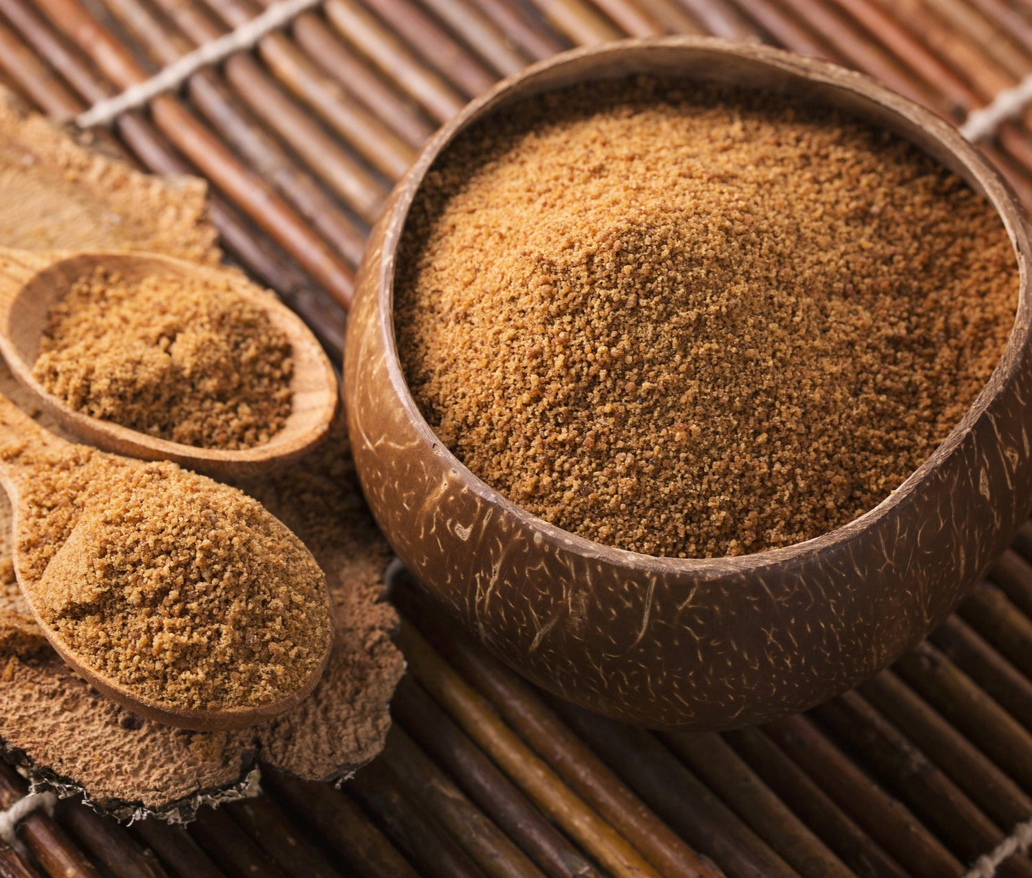 Coconut bowl and wooden utensils filled with unrefined coconut sugar, Sage Matcha's sweetener. On top of wooden mat.