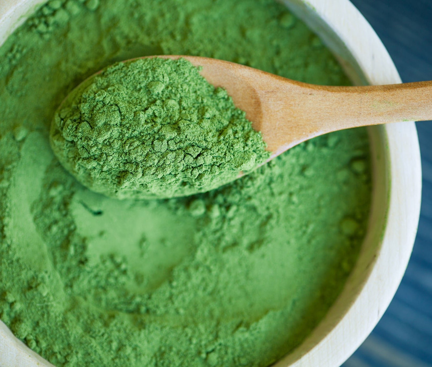 Green spirulina in a bowl, with some held up in a wooden spoon.