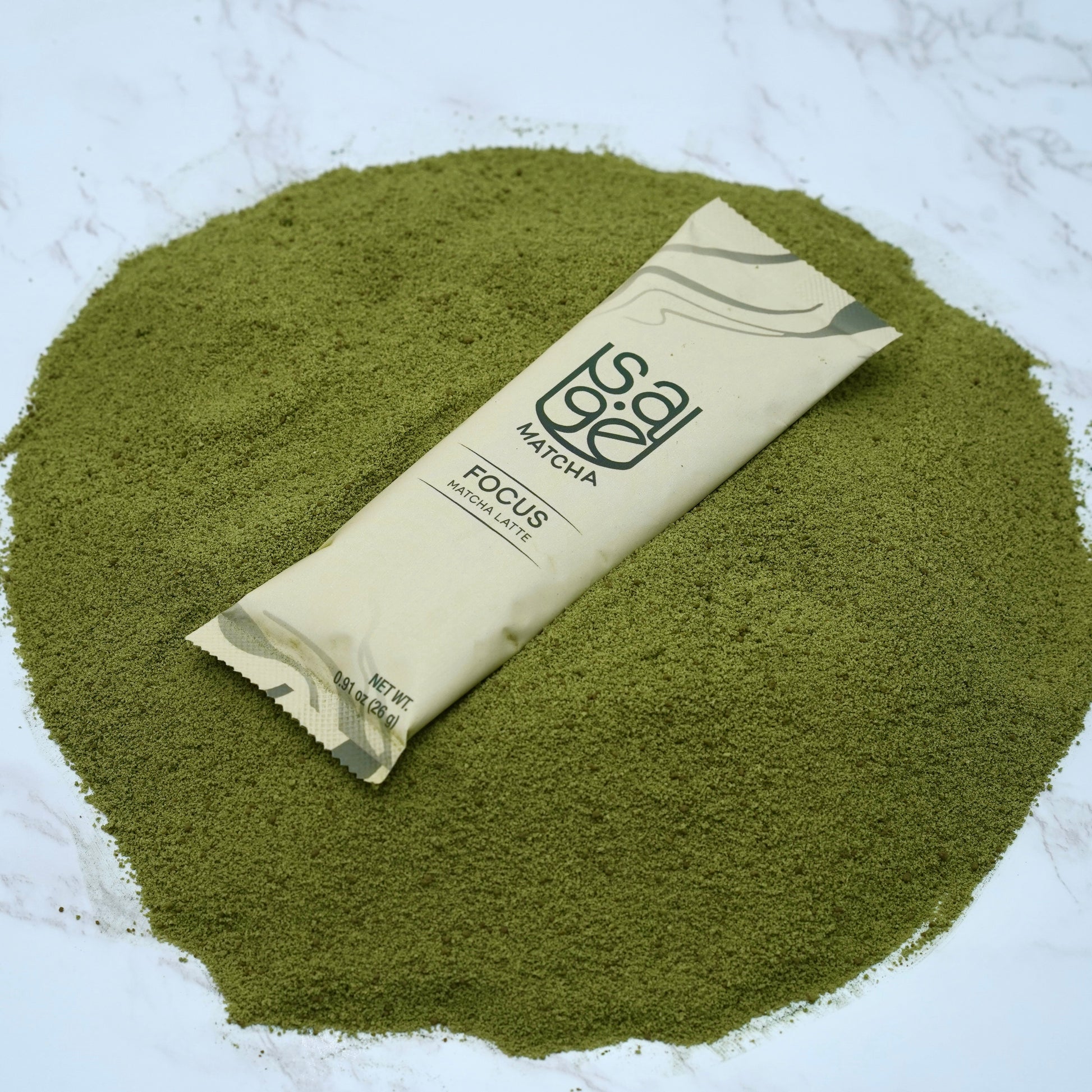 Single serving instant matcha latte Sage Matcha Focus blend on top of raw powder over marble countertop.