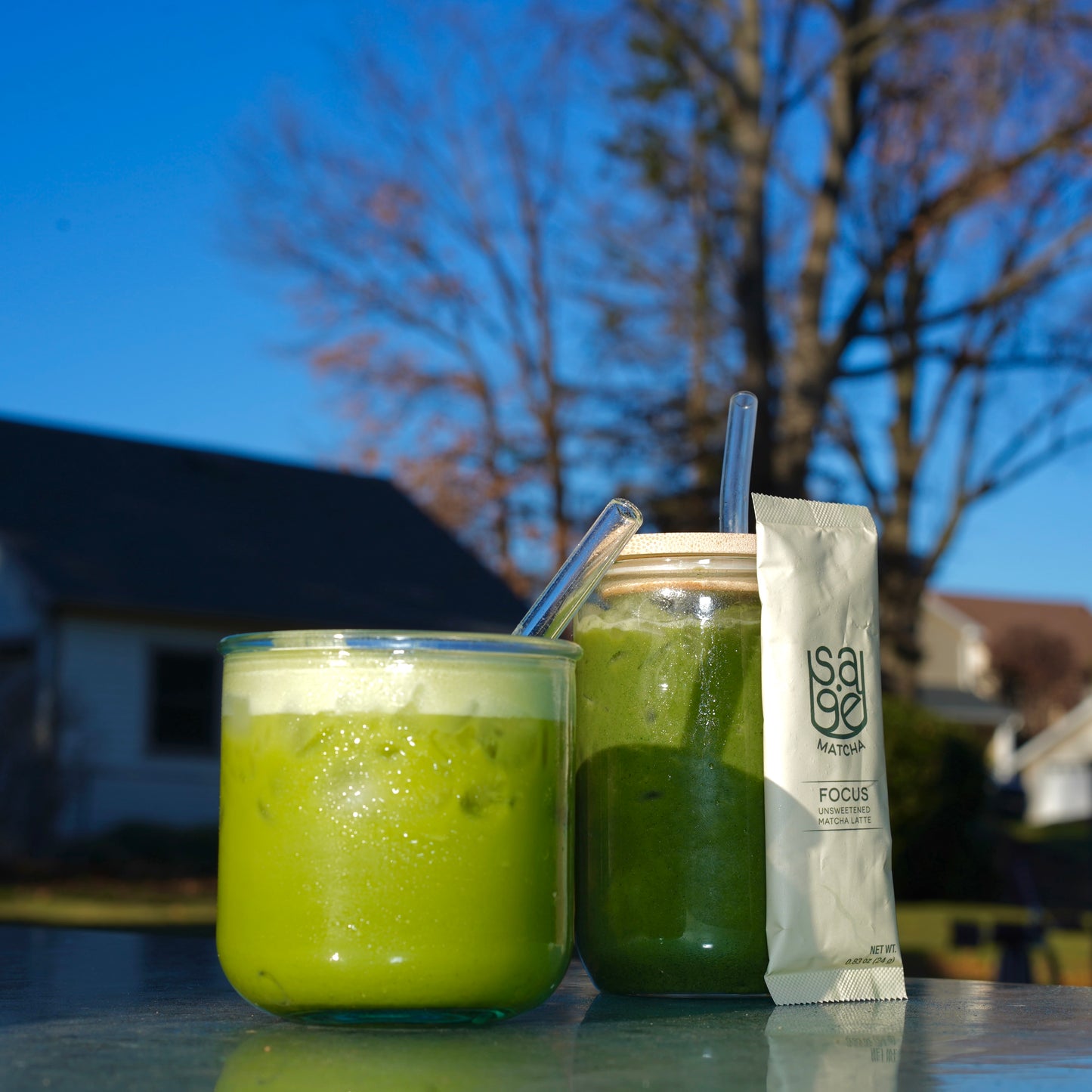 Two glasses of Sage Matcha instant lattes, Focus Unsweetened single serving stick leaning against one.