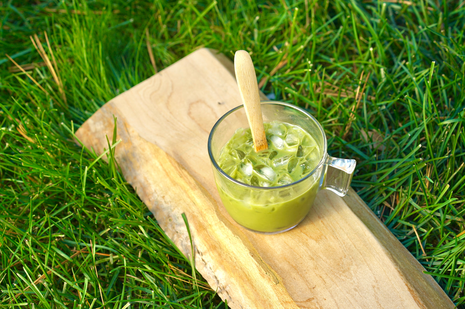 Matcha latte made from Sage Matcha, on wooden board, on grassy nature.