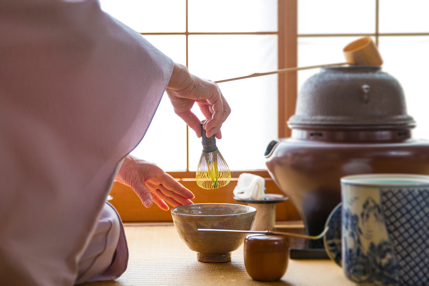 Woman's hands preparing a traditional matcha in a tea ceremony, holding whisk above bowl. 